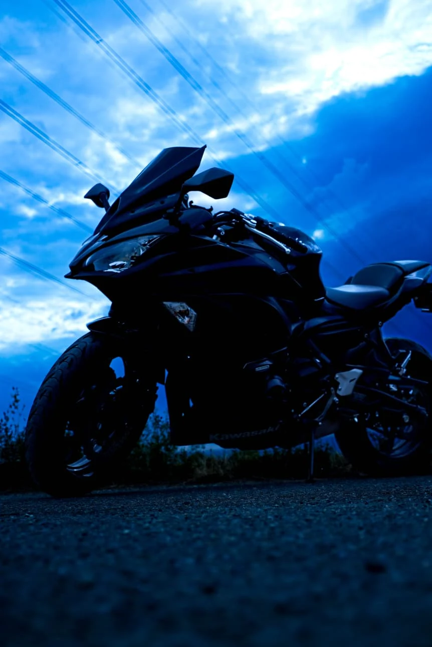 Kawasaki Ninja noire de trois quarts, sous un ciel bleu profond à l'heure bleue.