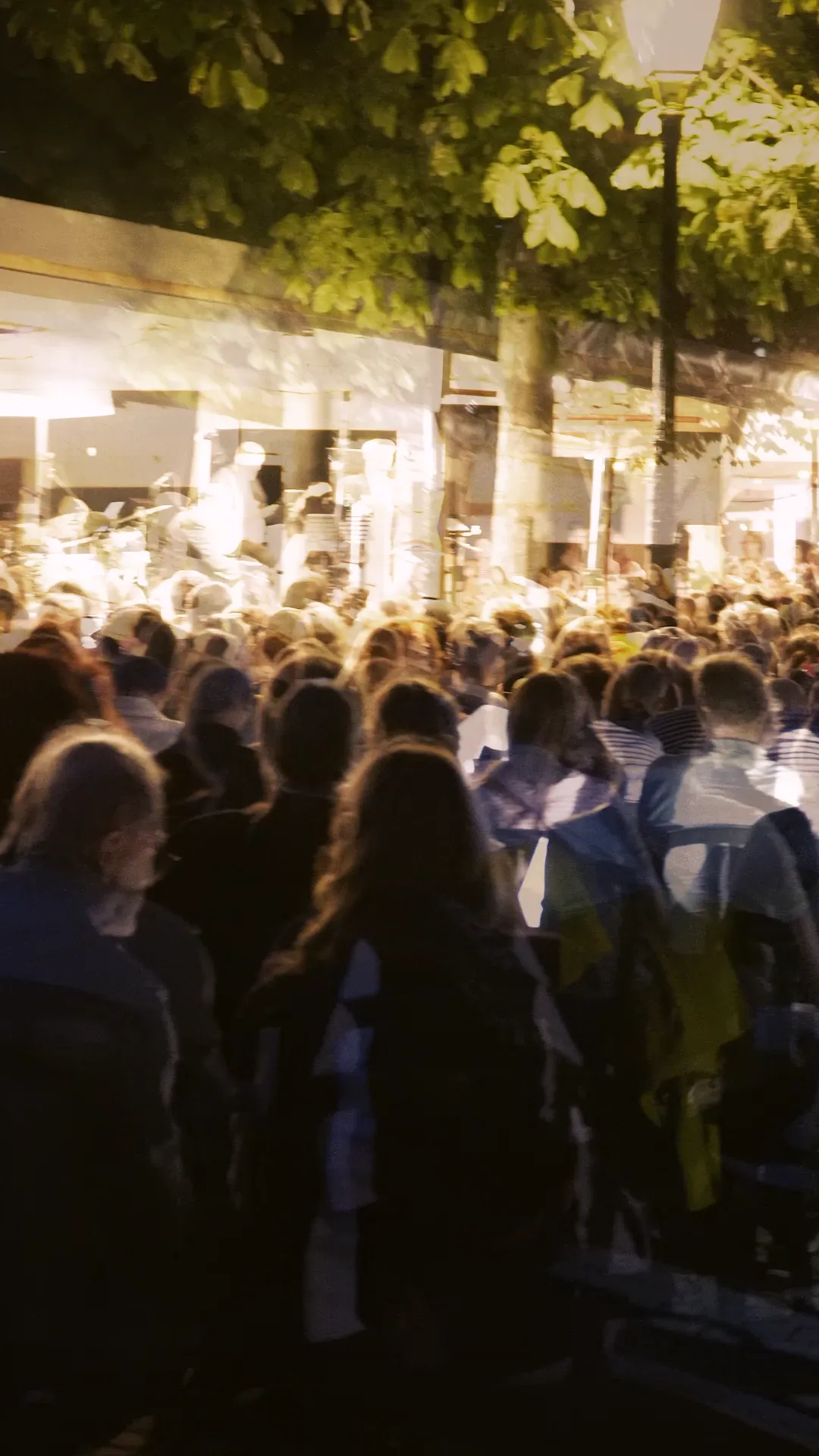 Image du film : la foule du chœur sous les lumières, à la tombée de la nuit.