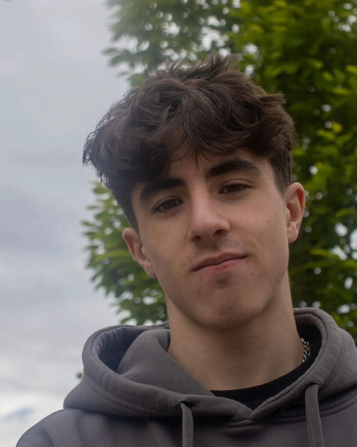 Portrait d'Ugo Martellotta, en sweat gris, devant un arbre.